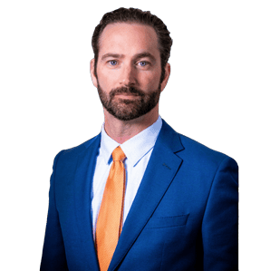 A man with a beard wearing a blue suit and orange tie stands facing forward against a white background.